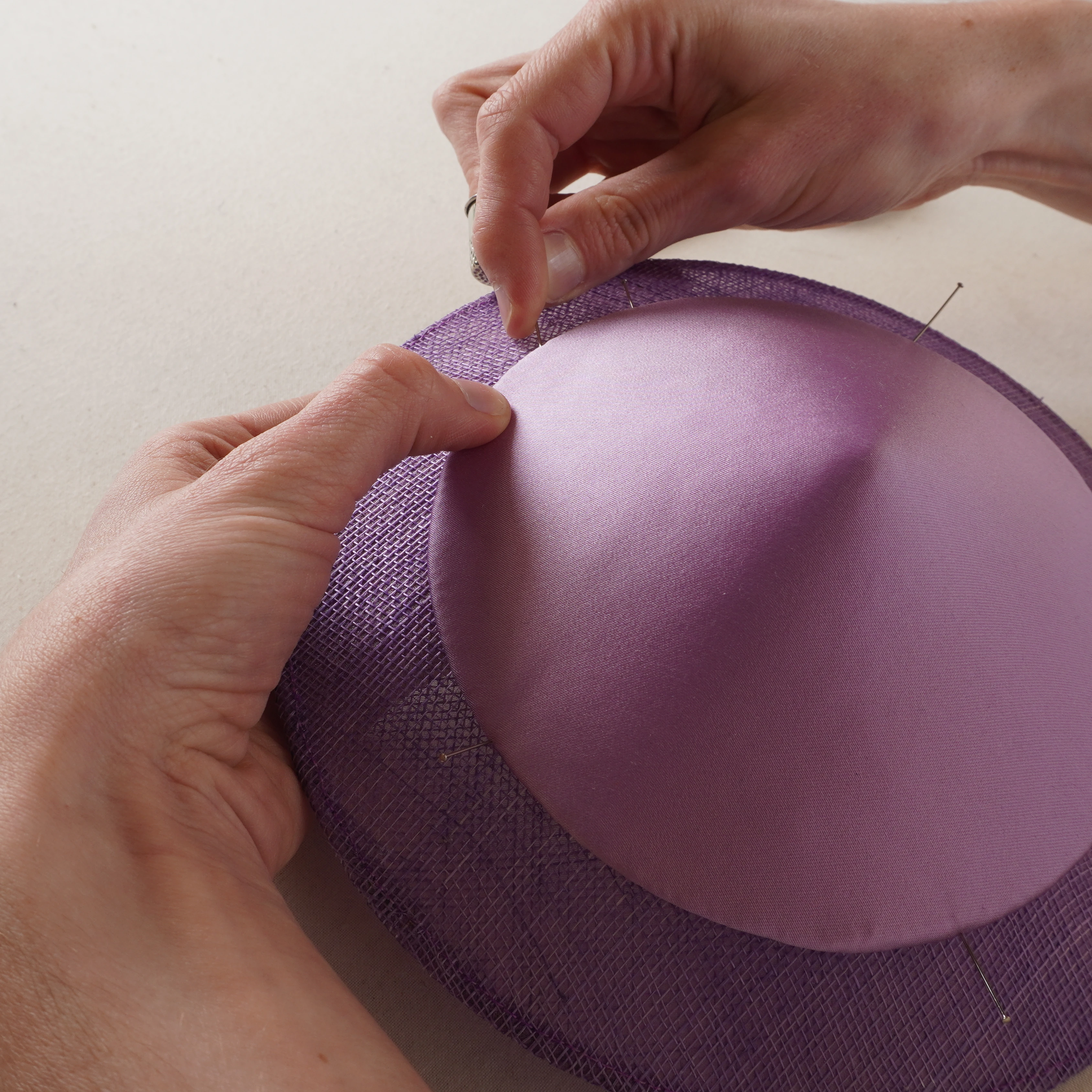 Montage &agrave; la main d'une calotte de satin mauve sur une base en sisal, maintenue par des &eacute;pingles